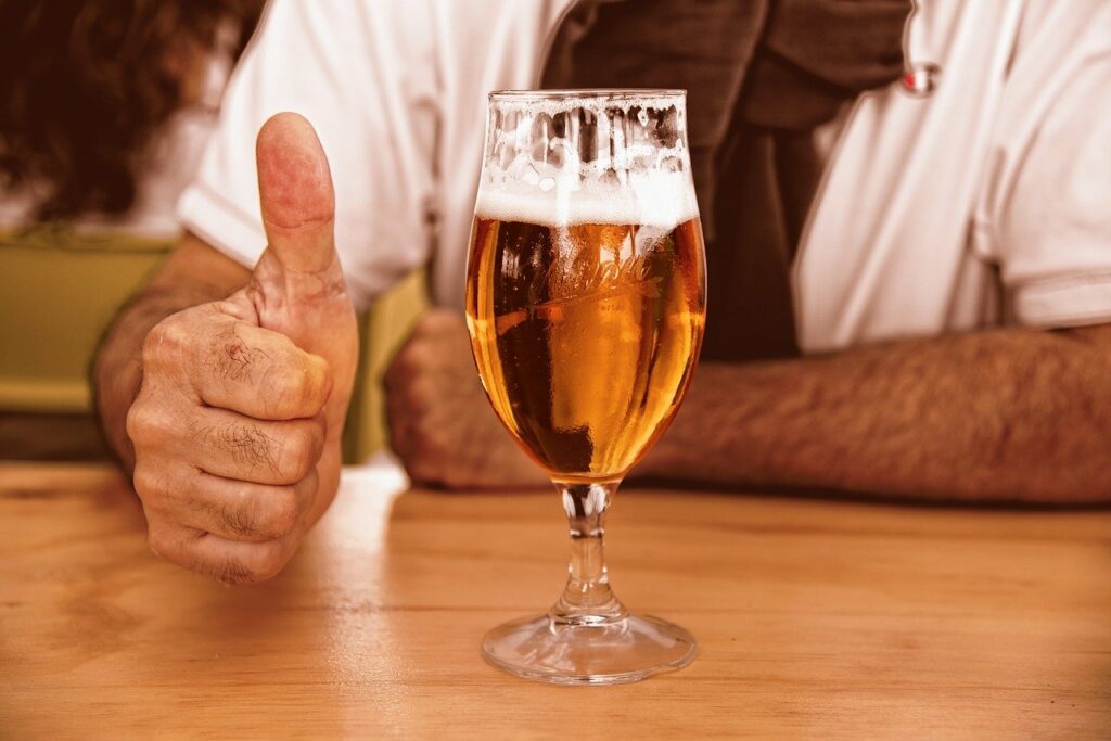 cerveja: a imagem mostra taça de cerveja em bancada com homem ao fundo fazendo sinal de "joia" com a mão